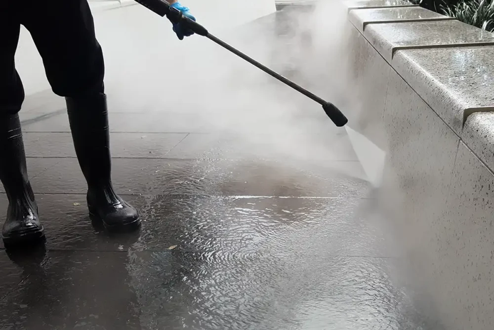 Man using pressure washing equipment on exterior stone surface